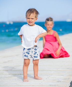 Cute toddler boy with his sister walking on jetty with turquoise sea