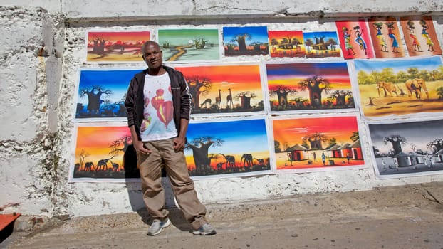 Cape Town, South Africa, December 4, 2011: South Africa is home to an estimated five-million illegal immigrants and the problem increases each day. Despite their qualifications, there is little work and much resentment for these illegal immigrants and some of them earn an income by creating African-themed art and curios. Here, a Malawian artist displays his colorful work at Kalk Bay Harbour, Cape Town.