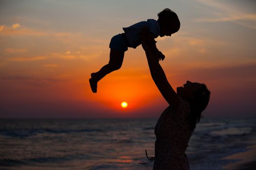 Mother and little son silhouettes on beach at sunset