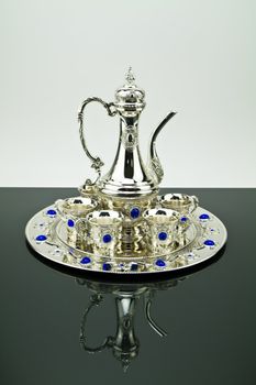 Silver tea set on the black mirror with mirror image