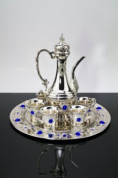 Silver tea set on a black mirror with white background
