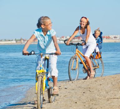Cute girl with her mother and brother ride bikes along the beach. Focus on mother