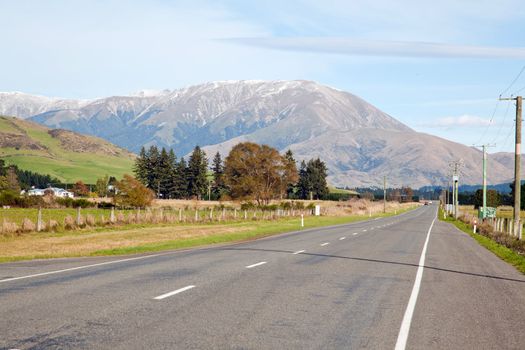 Long road stretching out into the distance with snow mountain background in New Zealand