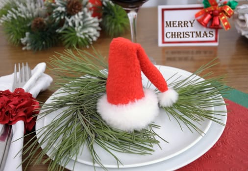 Christmas hat on a branch of pine in the plate on a festive table