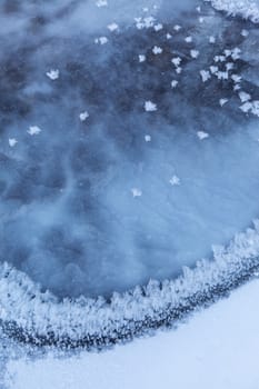 Image of frozen lake with ice edge covered with big icy snowflakes