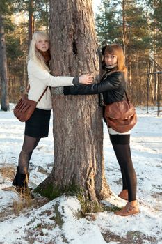 Two beautiful young girls embrace tree in wood
