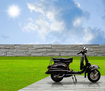 Black retro scooter parking in the garden with cloudy sky