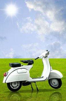 White retro vespa on grass in the garden with sky