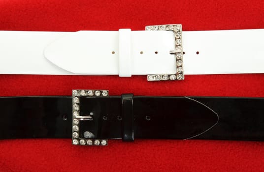 Two leather belts on red fabrics background