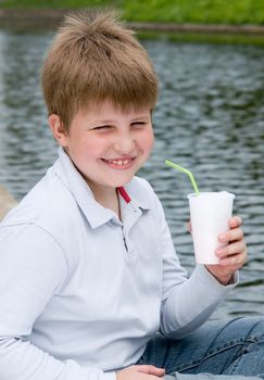 little boy drinks milkshake on a riverside