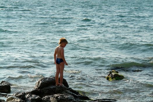 little boy on a rock in sea waves