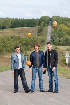 Three young men on road. Pumpkins fall from above.