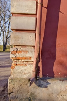 Old crumbling brick house corner wall closeup and rainwater pipe.