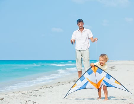 Little cute boy playing his father with a colorful kite on the tropical beach.