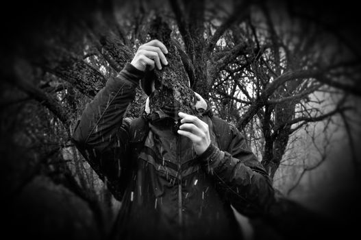Man under branches obscured with bark peel snow storm in forest. Black and white.