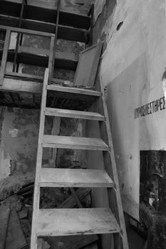 Wooden crumbling attic staircase and fire extinguisher sign in abandoned factory interior. Black and white.