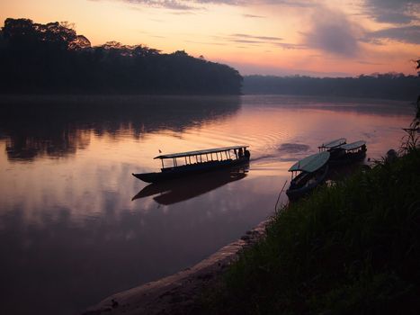 A boat navigating the Tambopata river during sunrise in the Amazon rainforest in Peru.