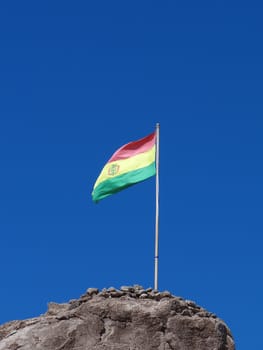 Flag of Bolivia on a mountain waving in the wind against a clear blue sky.