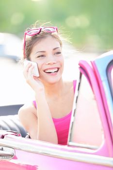 Vintage woman in retro car talking on mobile smart phone. Beautiful young mixed race woman driving in pink car smiling happy.