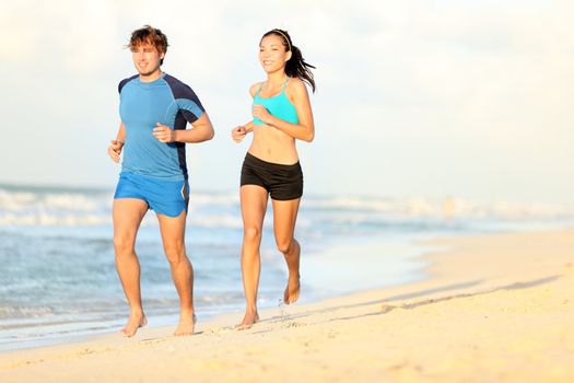 Couple running on beach. Runners jogging during outdoor workout on beautiful beach at sunset. Caucasian man, Asian woman.