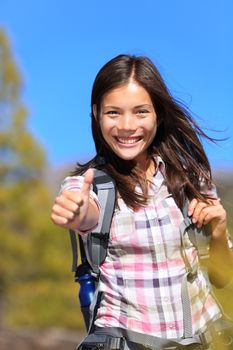 Hiking girl happy thumbs up smiling. Young Asian woman hiker smiling joyful at camera outdoor on hike trip. Beautiful young mixed race Asian Chinese / Caucasian woman walking in forest.