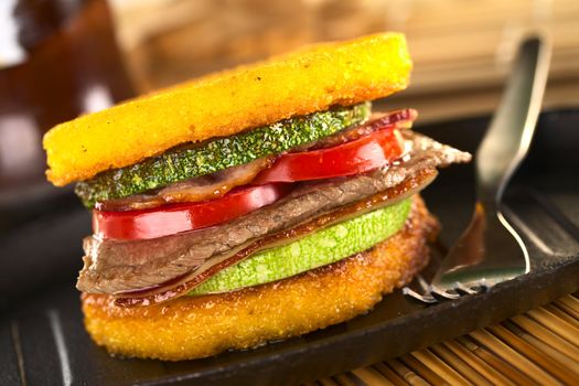 Polenta burger with fried zucchini, bacon, beef and tomato (Selective Focus, Focus on the front of the burger)