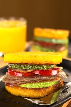 Polenta burgers with fried zucchini, bacon, beef and tomato accompanied by orange juice (Selective Focus, Focus on the front of the burger)