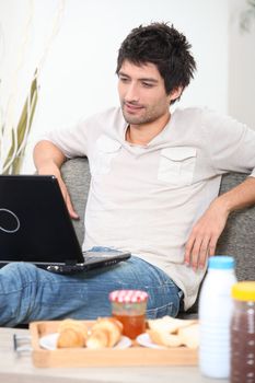 Man using a laptop computer in his front room with breakfast on a tray