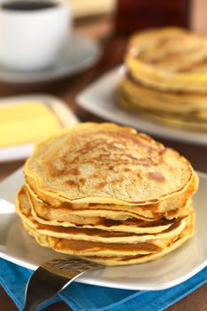 Fresh homemade pancakes with coffee, butter and maple syrup in the back (Selective Focus, Focus on the front of the upper three pancakes) 