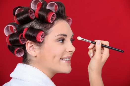 Woman with hair curlers applying make-up