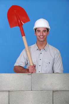 Man holding spade behind wall