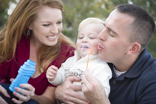 Attractive Young Parents Having Fun Blowing Bubbles with their Child Boy in the Park.