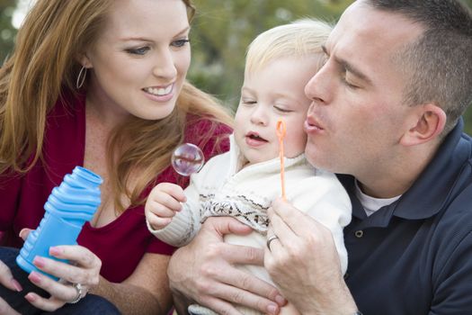 Attractive Young Parents Having Fun Blowing Bubbles with their Child Boy in the Park.