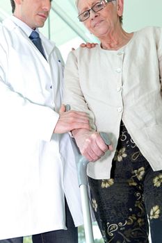 Doctor helping an elderly woman use a crutch