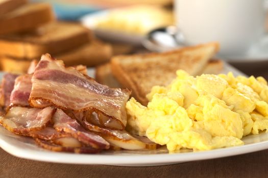 Fried bacon and scrambled eggs wth toast bread in the back (Selective Focus, Focus on the lower edge of the bacon on top) 