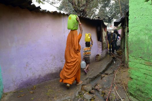 New Delhi,India-February 4, 2013:a woman and her son on the head door bins water in the slum on February 4,2013 in New Delhi. 17 million residents do not have access to city water