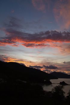 Sunset over the hills at Batu Ferringhi Penang Malaysia with silhouette of the hills and bay coastline in portrait orientation