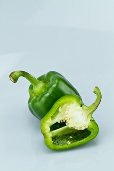 green capsicum with one cut open on bluish surface and background in portrait orientation