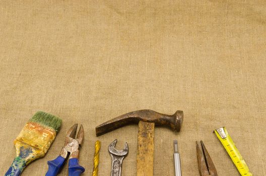 different retro rusty construction work tools hammer meter chisel wrench pincers screwdriver brush bit on linen cloth cloth background.