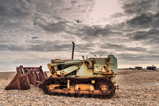 Rusty bulldozer on a shingle beach with a cloudy sky