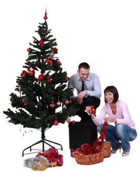 Studio shot of a young happy couple decorating the Christmas tree, against a white background.