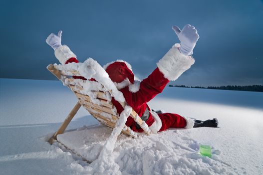 Santa claus relaxing on a sunbed in snow at night
