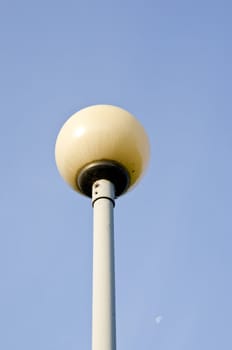 Glass ball on metal pole. Park illuminator and moon in sky.