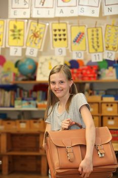 Happy girl at school with school bag. In the background of the classroom can be seen.