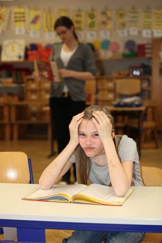 Overburdened student in the school. In the background is the teacher.