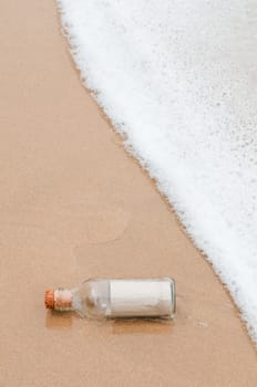 Brown paper in glass bottle near water edge of the beach.