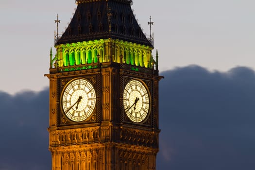 A fragment of the famous tower of Big Ben. The tower officially called the Elizabeth Tower. Close-up of the clock dials with night illumination of the building. Evening. London, UK.