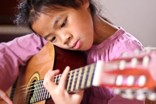 Cute girl playing guitar indoor with high concentration