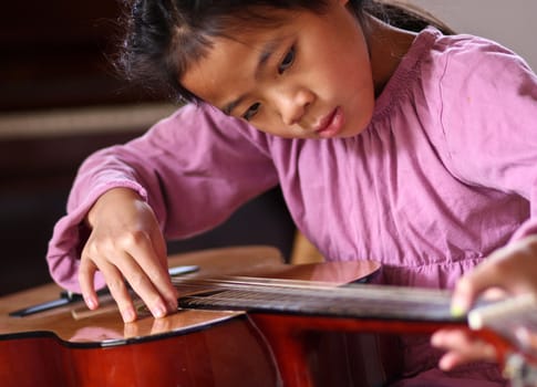 Cute girl playing guitar indoor with high concentration