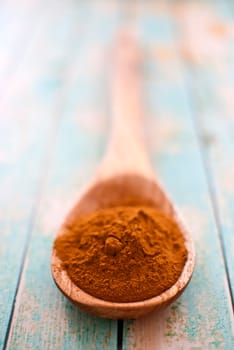 cinnamon powder in wooden spoon over wood background - selective focus